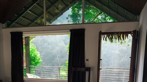 A room with a bed, a chair, a desk, and a large window with a view of greenery. - Eco Vista (Somvarpet)