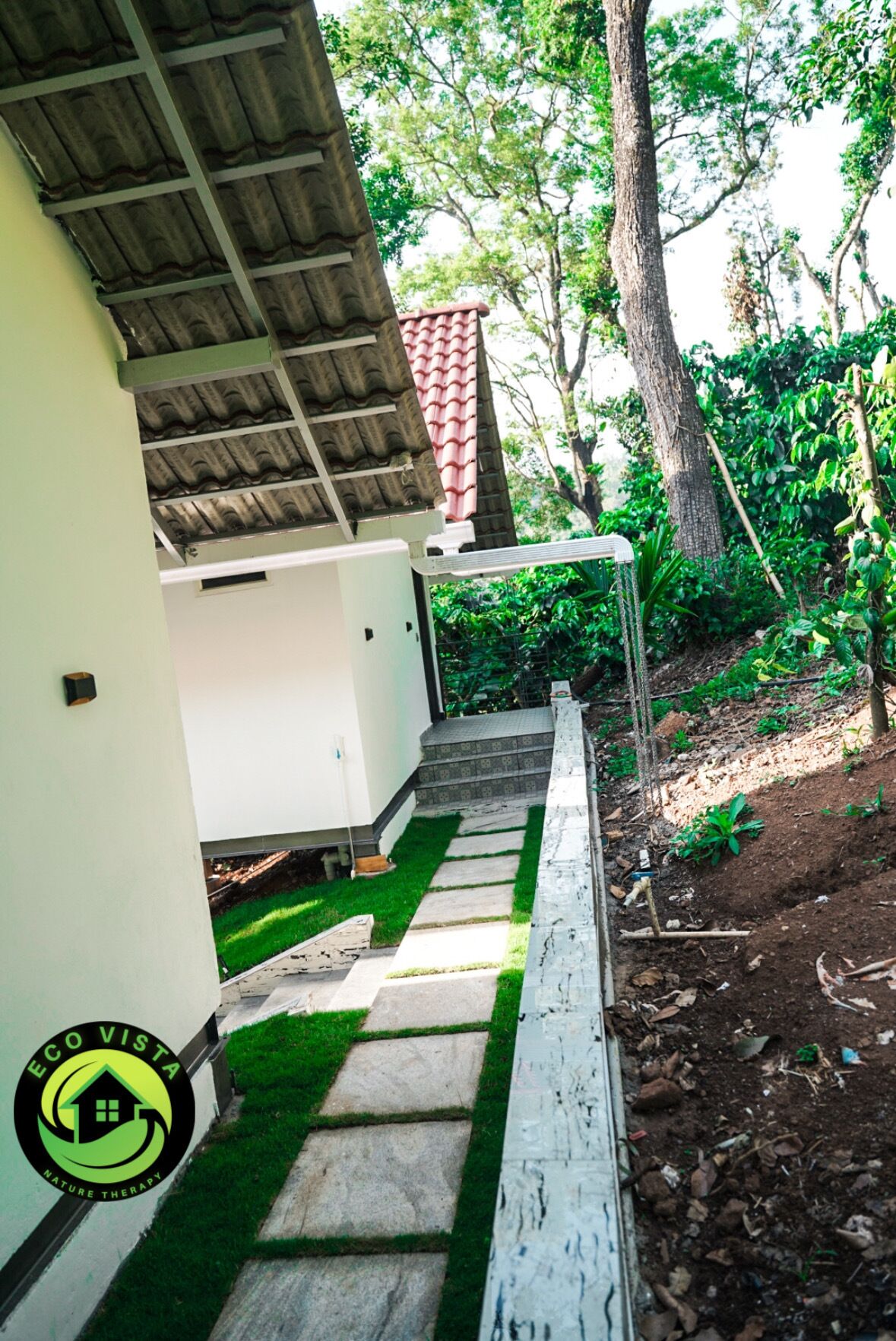 A pathway leading to a building with a tiled roof and a small garden area with grass and plants.