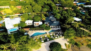 An aerial view of a resort with a large pool, multiple buildings, and lush greenery.