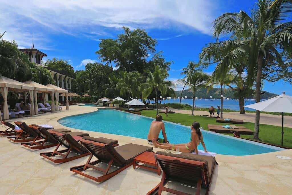 A poolside area with lounge chairs, umbrellas, and a view of the sea.