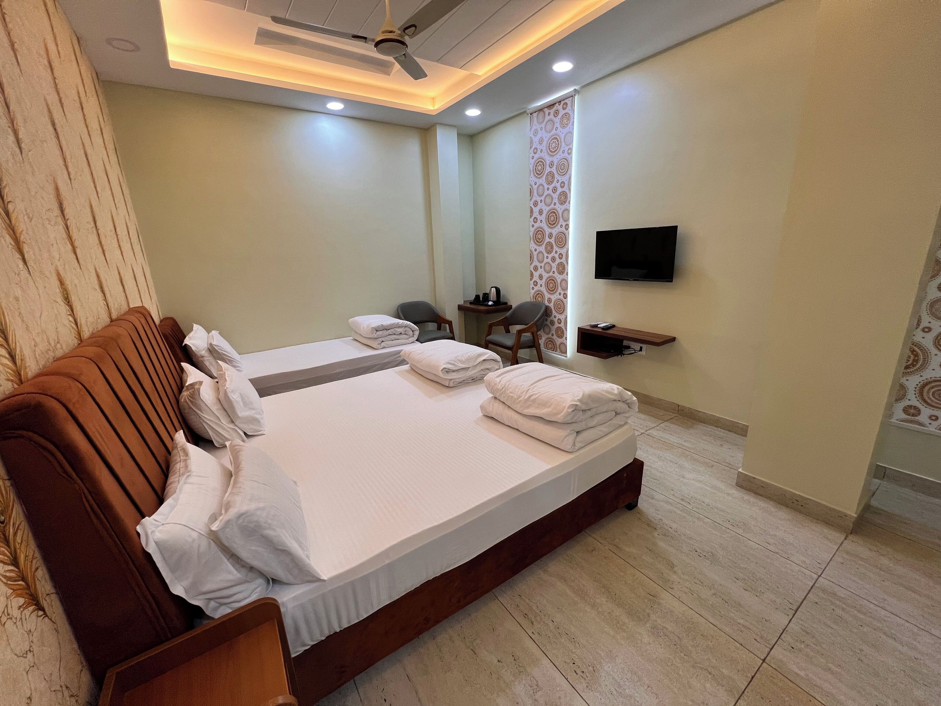 Habitación de hotel con una cama grande, un ventilador de techo, un televisor montado en la pared y una pequeña mesa con una silla.