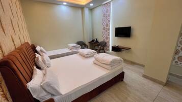 Habitación de hotel con una cama grande, un ventilador de techo, un televisor montado en la pared y una pequeña mesa con una silla.