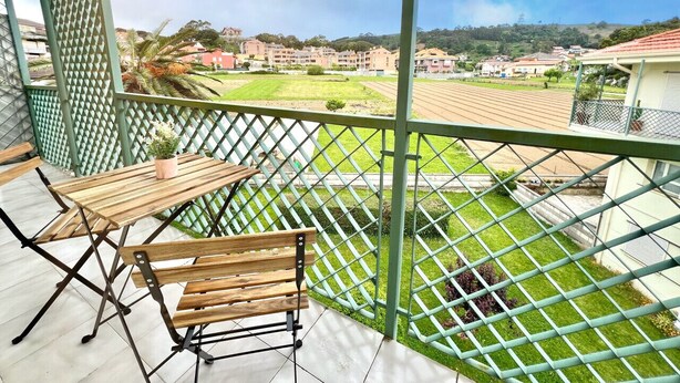 A balcony with a wooden table and bench, a green lattice fence, and a view of a residential area with houses and greenery. - Comfortable apartment near the beach (Isla)