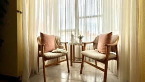 A room with two wooden chairs with cushions, a small table with a pitcher and a plant, and sheer curtains. - Comfortable apartment near the beach (Isla)