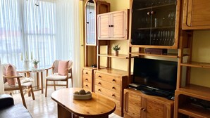 A cozy living room with wooden furniture, a television, and a dining area with chairs and a table. - Comfortable apartment near the beach (Isla)
