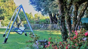 Un columpio en un jardín con un muro de piedra y arbustos florecientes.