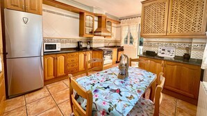 Una cocina con armarios de madera, un refrigerador de acero inoxidable, un microondas y una mesa de comedor con mantel floral.