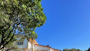 Una casa de dos pisos con un balcón, rodeada por un césped cuidado y un muro de piedra.