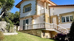 Una casa de dos pisos con un balcón, un muro de piedra de contención y un césped cuidado.