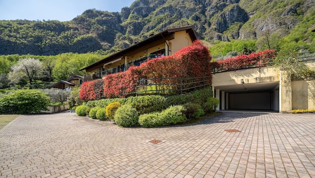 A building with a paved driveway, surrounded by well-maintained hedges and flowering plants.