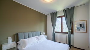 A bedroom with a bed, a nightstand, a window with curtains, and a radiator.