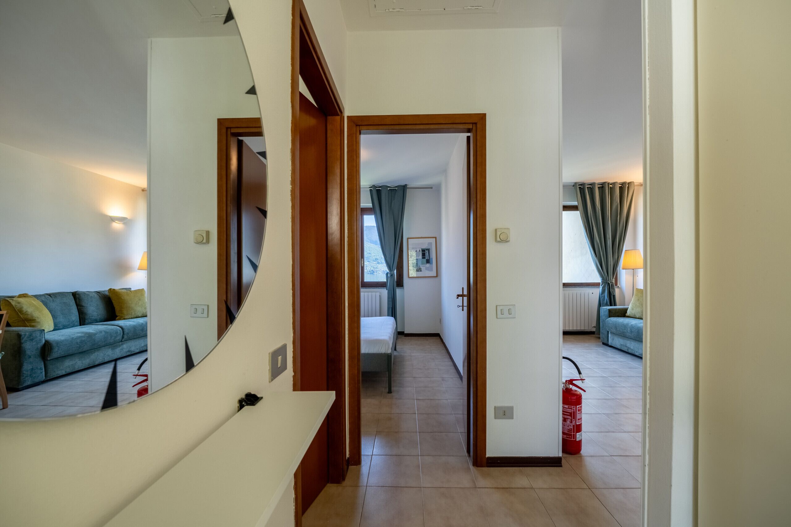 Un passadís que condueix a una habitació amb un llit, una finestra amb cortines i un extintor a terra.