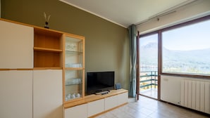 A modern living room with a TV, wooden shelves, and a view of mountains through a large window.