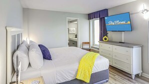 Een slaapkamer met een bed, een dressoir, een televisie en een raam met gordijnen.