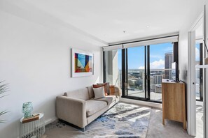 A modern living room with a sofa, a coffee table, and a view of the city through large windows. - Prime Location! Pool, Gym, Tower Views | Zodiak (Auckland)