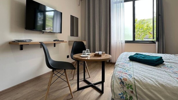A hotel room with a bed, a TV mounted on the wall, a small round table with chairs, and a window with curtains. - Tikhii Zamok (Bishkek)