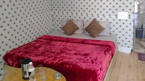 Une pièce aménagée avec une tente, un lit, des oreillers, une couverture rouge, une petite table en bois avec une bouilloire et des verres, et un luminaire suspendu.