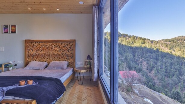 Ein Schlafzimmer mit einem großen Bett, einem Holzkopfende, einem kleinen Tisch und Blick auf einen bewaldeten Hügel.