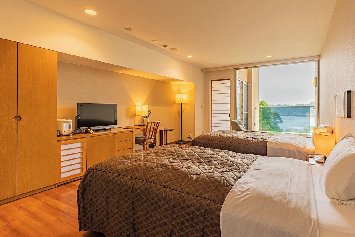 A hotel room with two beds, a desk with a television, and a view of a lake.