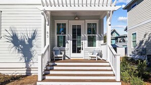 A white house with a covered porch, steps leading to a door, and two chairs on the porch.