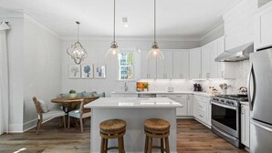 A modern kitchen with white cabinetry, a central island with stools, pendant lighting, and stainless steel appliances.