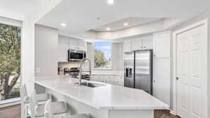 A modern kitchen with white cabinetry, stainless steel appliances, and a large island with bar stools. - St Lucia 306*Guest Favorite*HighEnd*ResortAmenites (Destin)