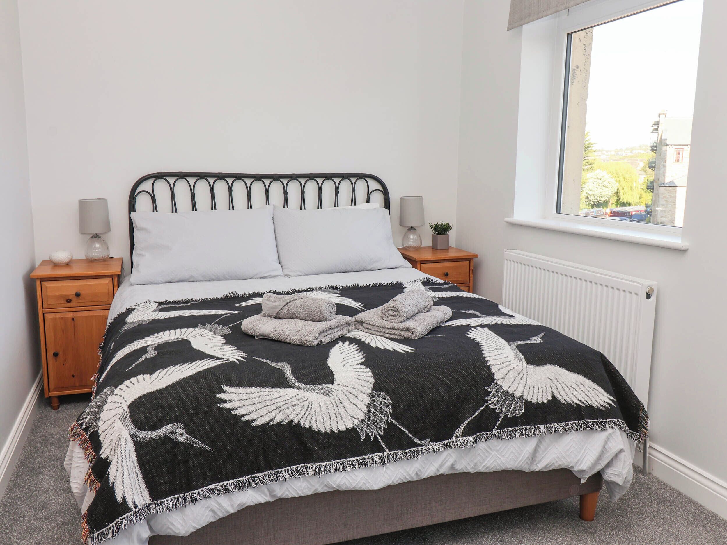 A neatly made bed with a black and white feathered blanket, two bedside lamps, and a window with a view of the outside.