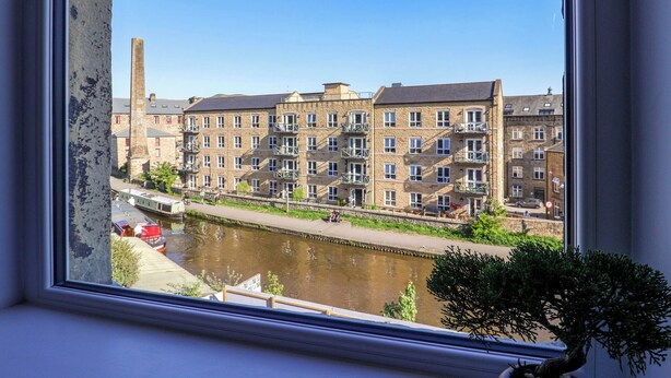 A view of a riverside building with multiple floors, balconies, and a narrow waterway in front. - Canal View (Skipton)