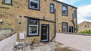 A stone building with multiple windows and a door, a small outdoor seating area with plastic chairs, and a paved ground. - Canal View (Skipton)