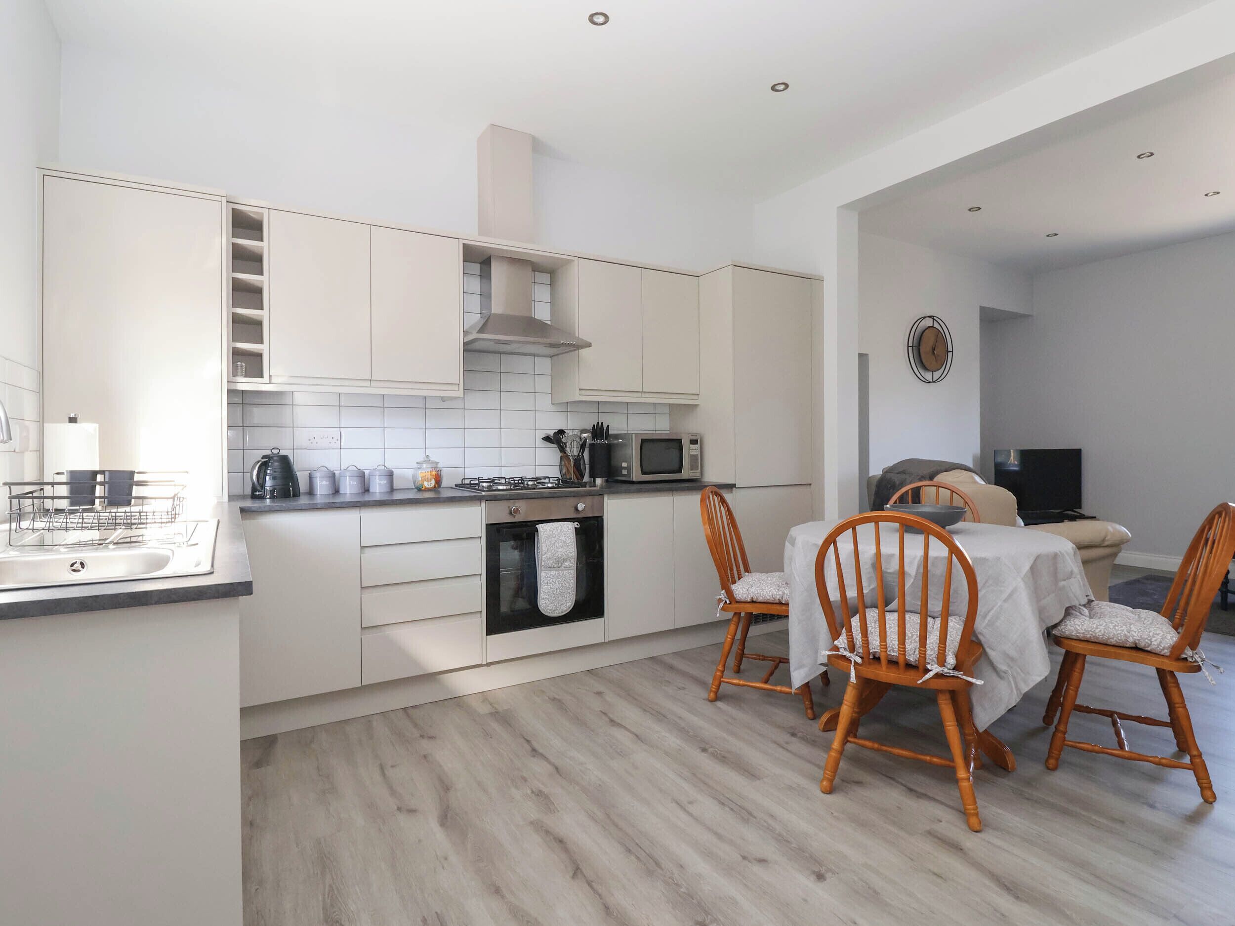 Une cuisine moderne avec des meubles blancs, un four à micro-ondes et un coin repas comprenant des chaises et une table en bois.
