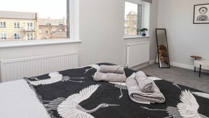 A bedroom with a large window, a radiator, a bed with a black and white feathered blanket, and a mirror on the wall. - Canal View (Skipton)