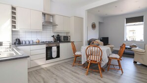 A modern kitchen with white cabinets, a microwave, and a stove. There is a dining area with a table and chairs. - Canal View (Skipton)