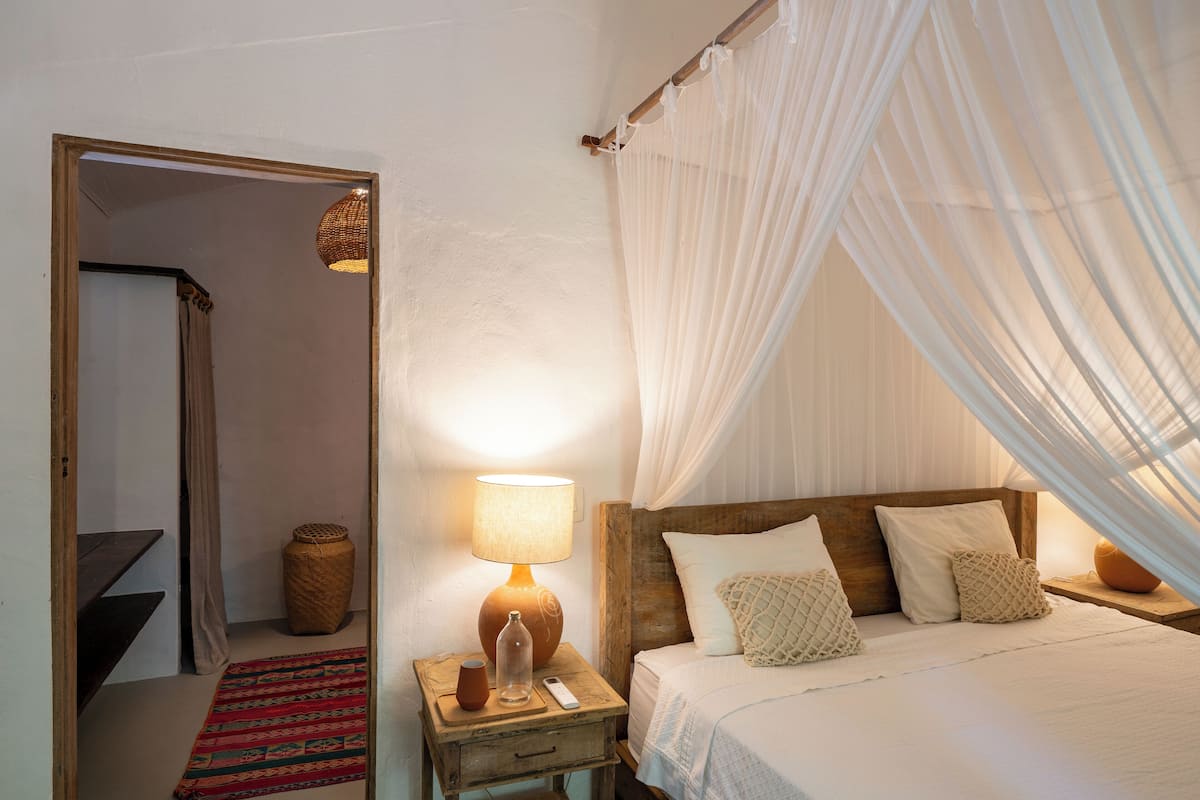 Una camera da letto con testiera in legno, letto a baldacchino, comodino con lampada, un vaso e un piccolo tappeto.