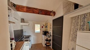 A narrow kitchen with a tiled floor, a wooden ceiling beam, a black door, and a white refrigerator.