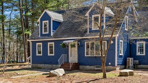 A two-story blue house with a front porch, a small staircase, and a large window.