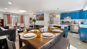 A modern kitchen with blue cabinets, a dining area with a wooden table set for four, and a living room with a sofa and a coffee table.