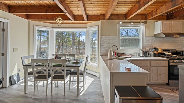 A modern kitchen with a large island, wooden beams, and a view of trees through the windows. - Cozy Riverfront Stay in Wareham (Wareham)