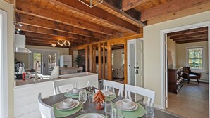 A dining area with a wooden ceiling, a kitchen in the background, and a view of a living room. - Cozy Riverfront Stay in Wareham (Wareham)