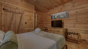 Un dormitorio de cabaña de madera con una cama, un televisor y un cuadro de un bosque en la pared.
