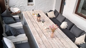 Een terras met een houten tafel, beklede banken en een hangstoel.