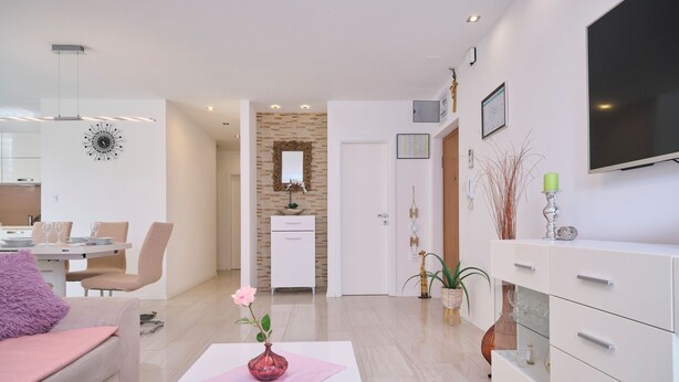 Ein modernes Wohnzimmer mit einem weißen Sofa, einem Couchtisch mit einer rosafarbenen Vase und einem Essbereich mit einem weißen Schrank und Stühlen.