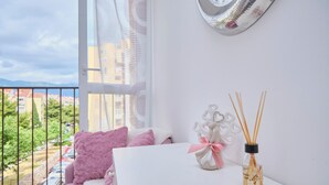 Ein Zimmer mit einem weißen Tisch, rosa Kissen, einem dekorativen Gegenstand und einer Flasche mit Rattan-Diffusor.