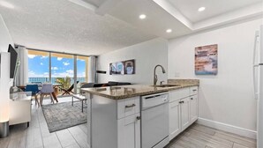 A modern kitchen with a large island, white cabinetry, and a view to a balcony.