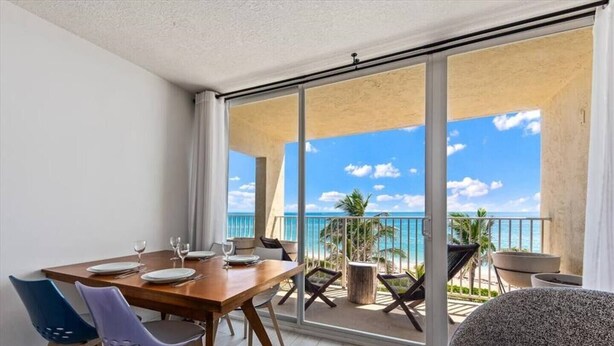 A balcony with a dining table set for two, a chair, and a sofa.