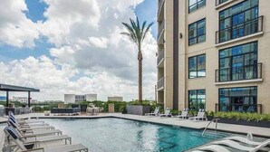 A rooftop pool with lounge chairs, a palm tree, and a modern building with large windows. - Houston Gem: Walk to Med Center & NRG (Houston)