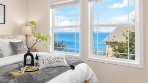 Une chambre à coucher avec un lit, une table de chevet, une lampe, une plante et une fenêtre donnant sur la mer.