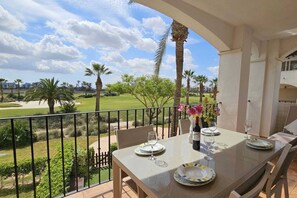 A balcony with a table set for dining, overlooking a golf course and palm trees. - Beautiful 2 bed apartment at La Torre Golf AO711LT (Murcia)