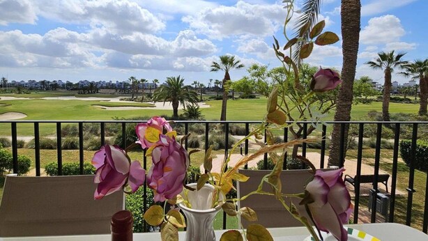 A balcony with a view of a golf course, a vase with flowers, and a table with chairs. - Beautiful 2 bed apartment at La Torre Golf AO711LT (Murcia)