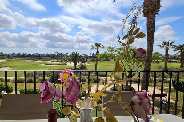 Un balcon donnant sur un terrain de golf, un vase rempli de fleurs et une table avec des chaises.