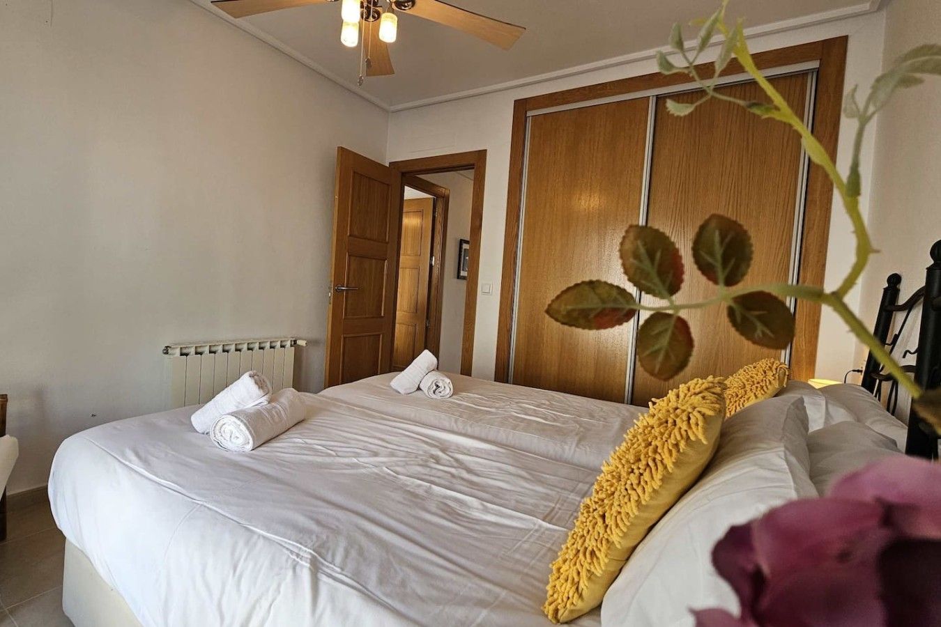 A hotel room with a bed, a radiator, a wooden wardrobe, and a ceiling fan.